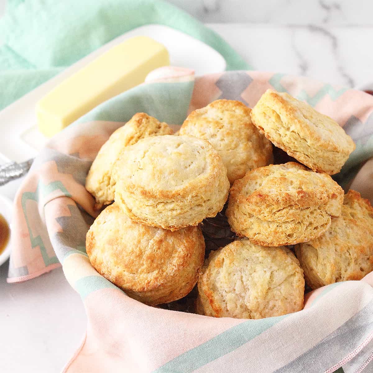 Head on shot of old fashioned buttermilk biscuits in basket with napkin line and butter in back.