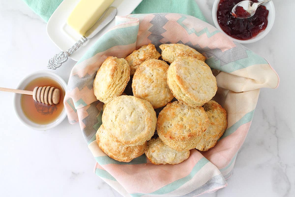 Overhead of biscuits in basket with napkin liner and jelly honey and butter beside them.