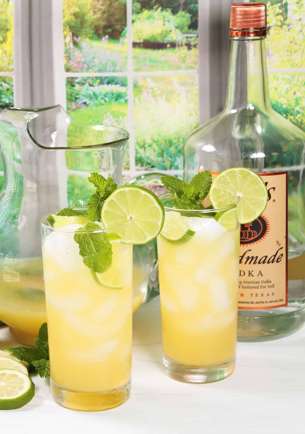 Two garnished vodka lime cocktails in front of window.