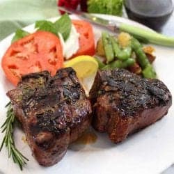 Closeup of plated lamb chops with green vegetables and caprese salad.