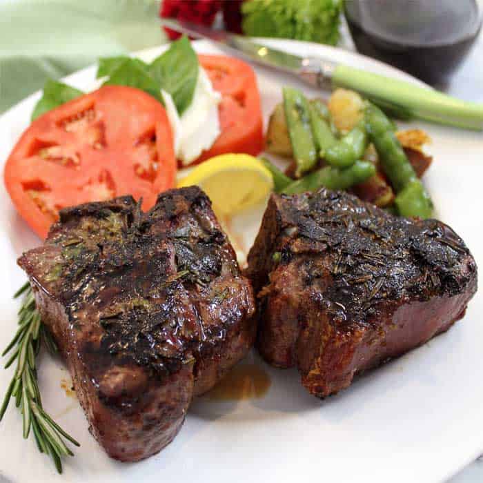 Closeup of plated lamb chops with green vegetables and caprese salad.