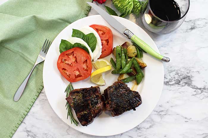 Overhead of dinner on white plate with glass of red wine and green napkin.