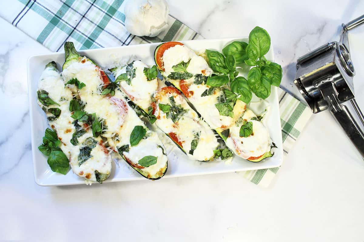 Zucchini boats pllated on white plate with basil garnish and cheese grater to side.