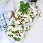 Zucchini boats on white plate with green plaid towel on side.
