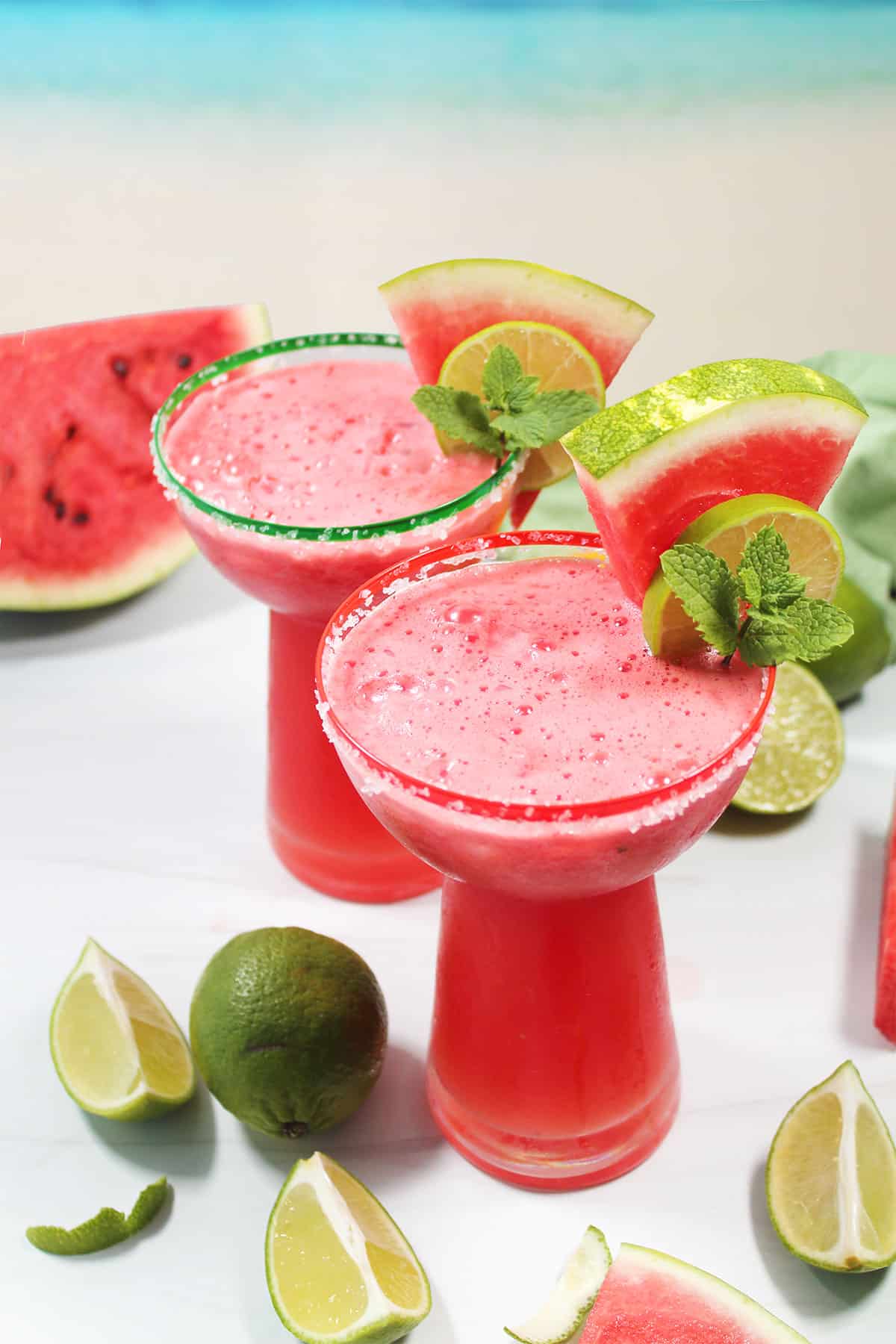 Two watermelon margaritas with watermelon wedge, lime and mint garnish.