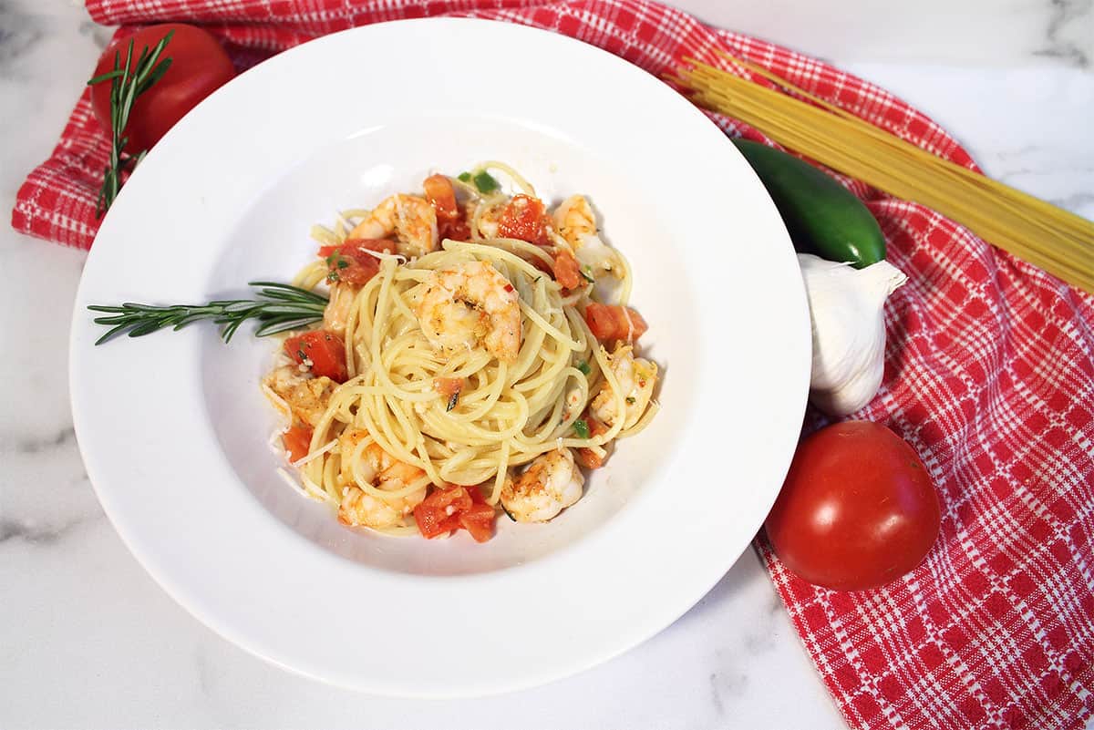 Overhead of pasta in white dish with tomato jalapeno garlic and pasta beside it.