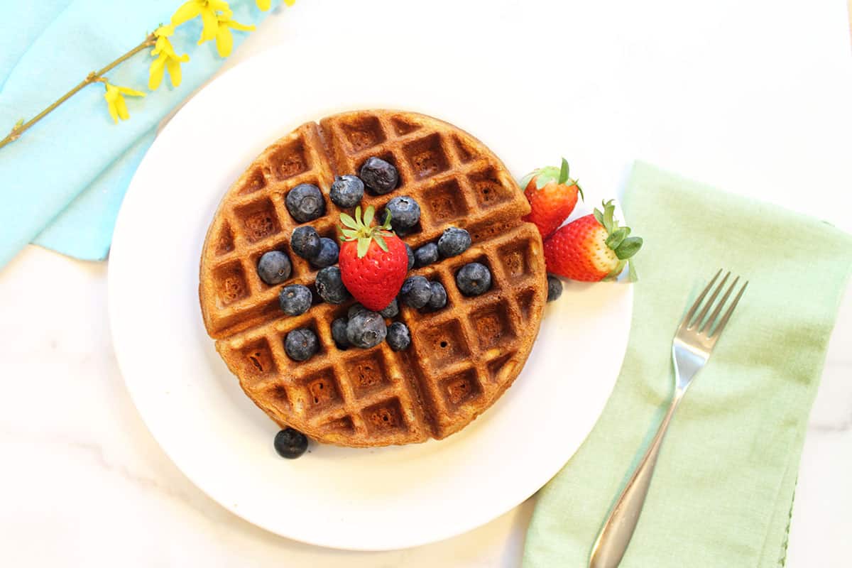 overhead view of almond waffles on white plate with berries on top.
