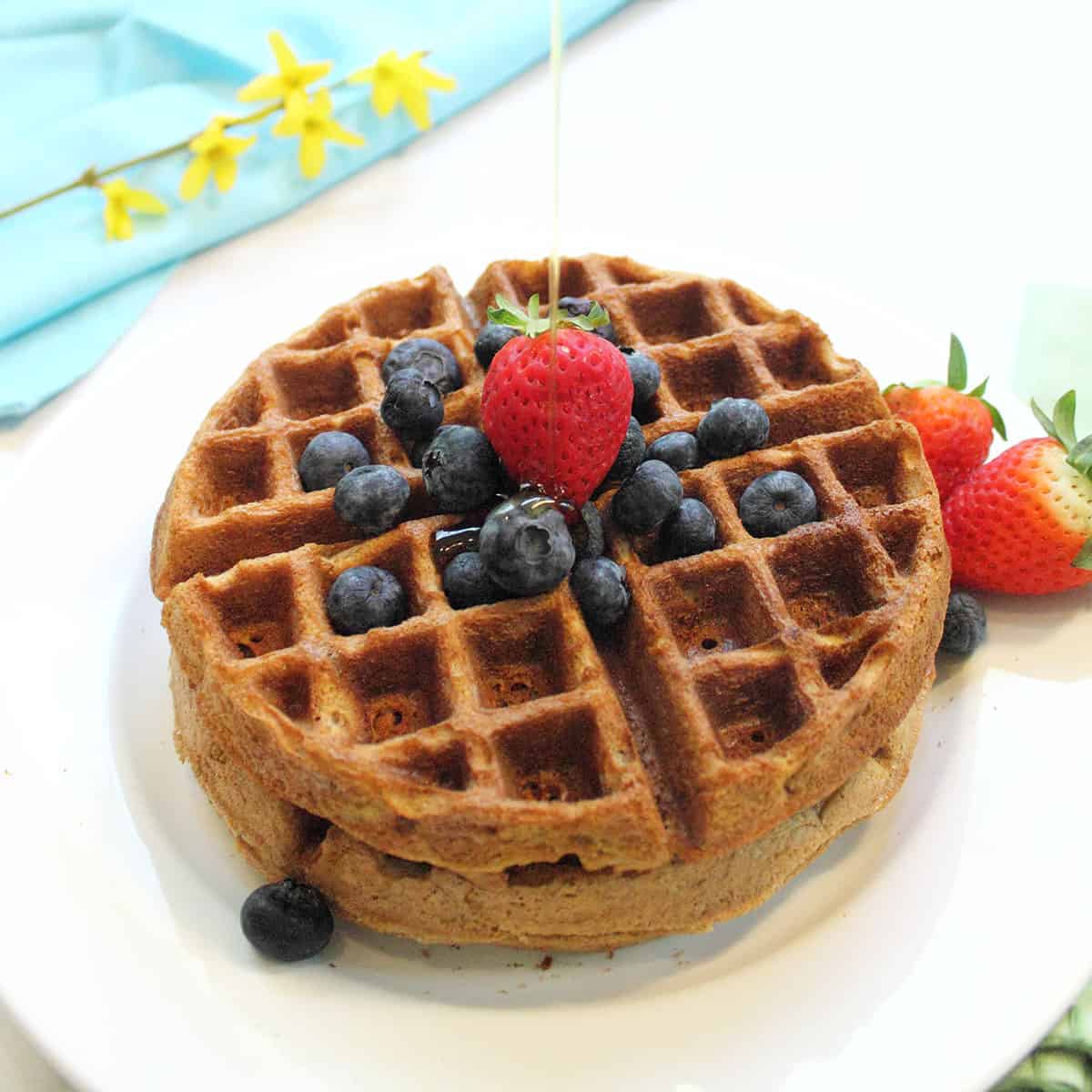 Pouring syrup on waffles on white plate.