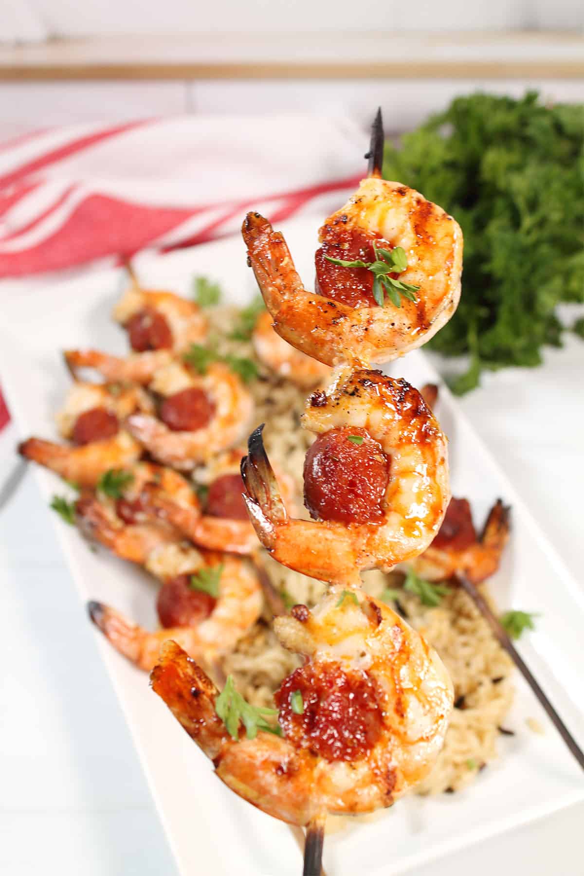 Holding grilled shrimp and chorizo skewers over platter.