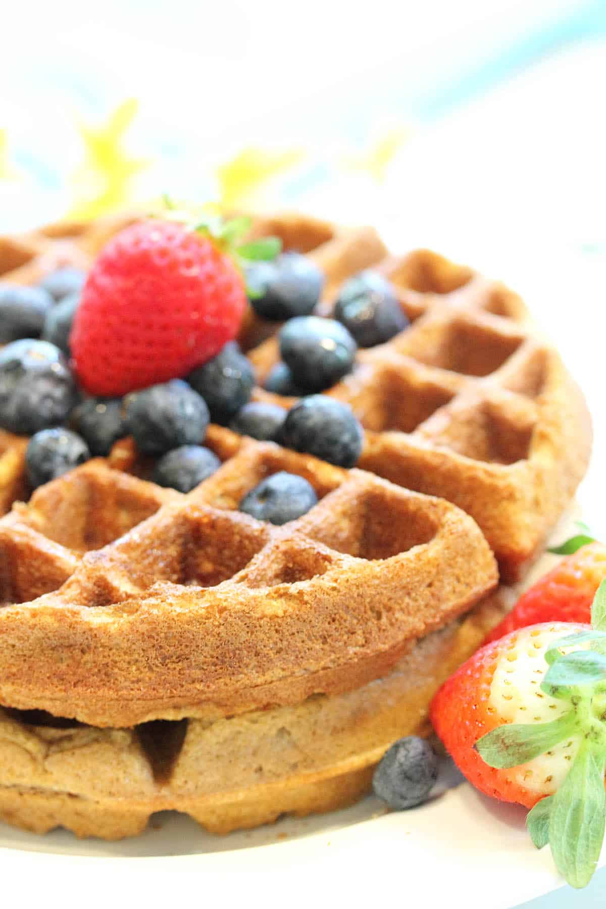 Side view of stacked almond waffles topped with blueberries and strawberry.