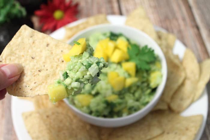 A bite of Mango Pineapple Guacamole on tortilla chip.