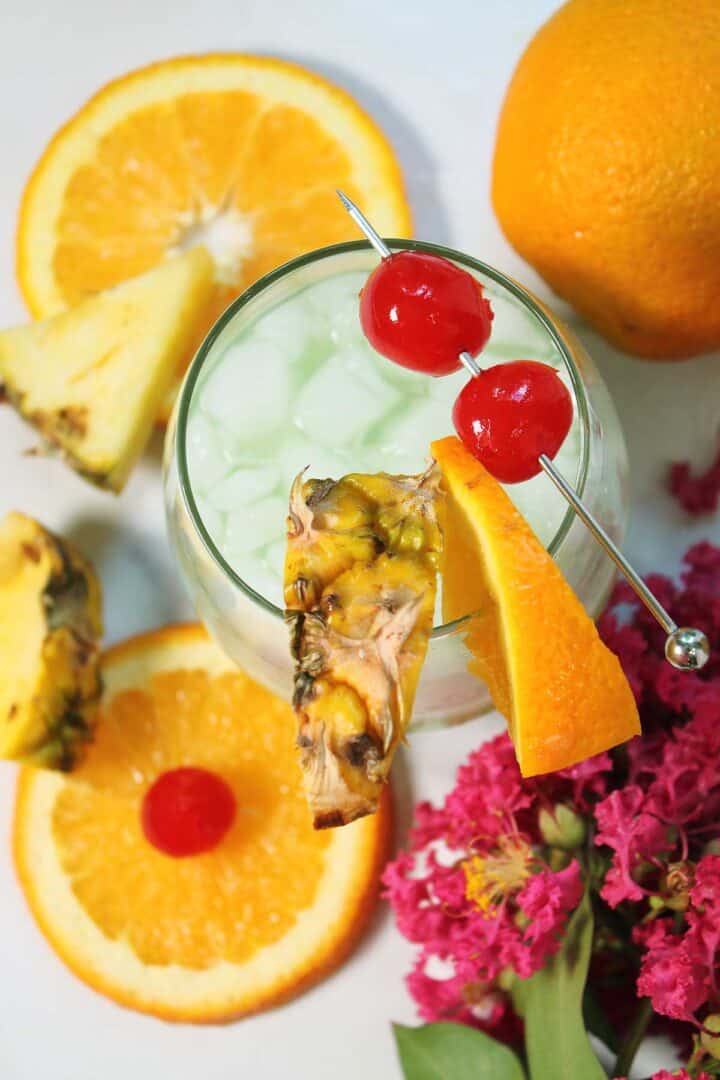 Looking down on blue cocktail with garnish of pineapple and cherries.