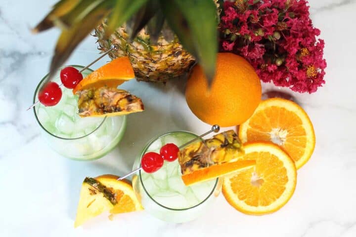 Overhead of two granished cocktails looking through pineapple leaves.