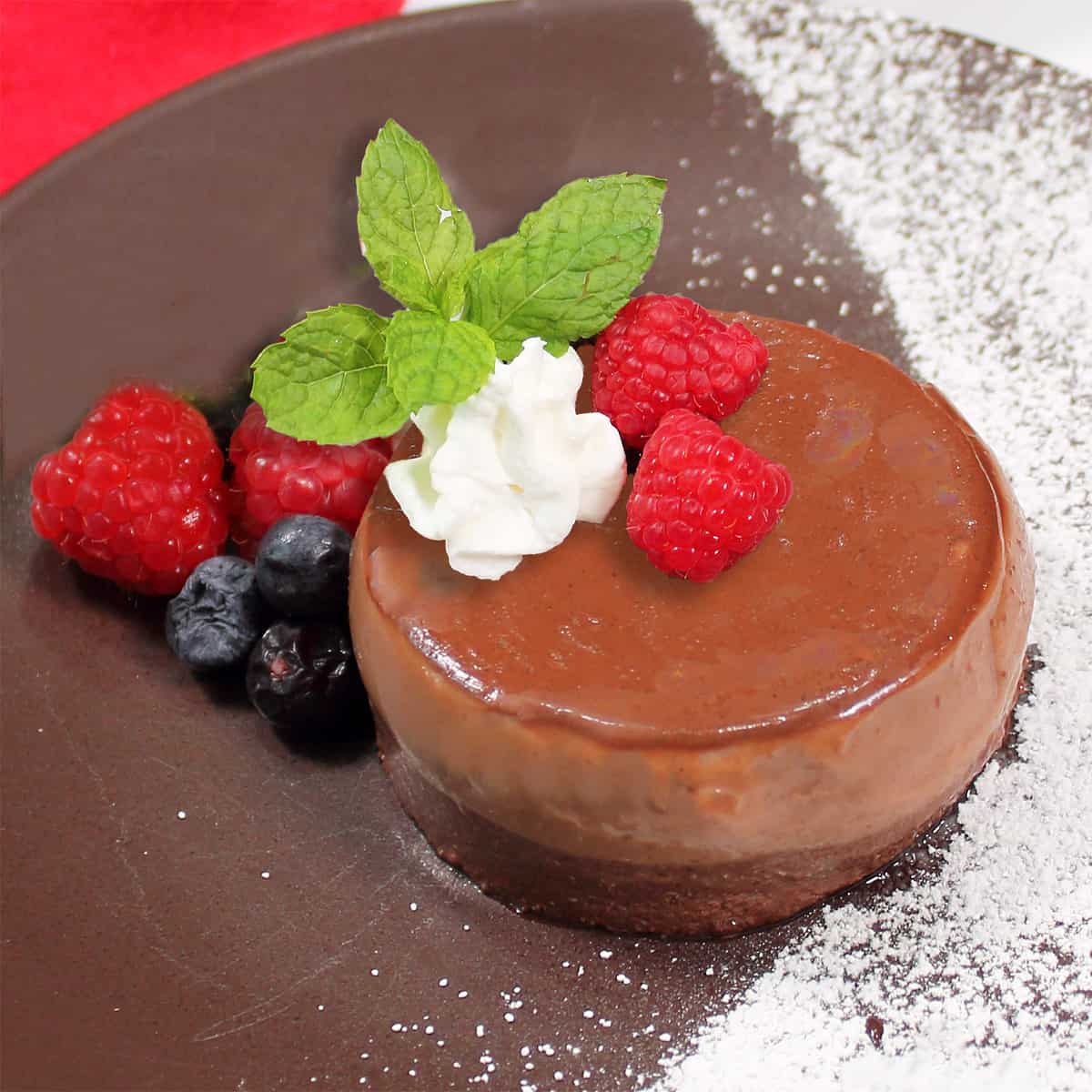 Plated panna cotta garnished with berries, shipped cream and mint.