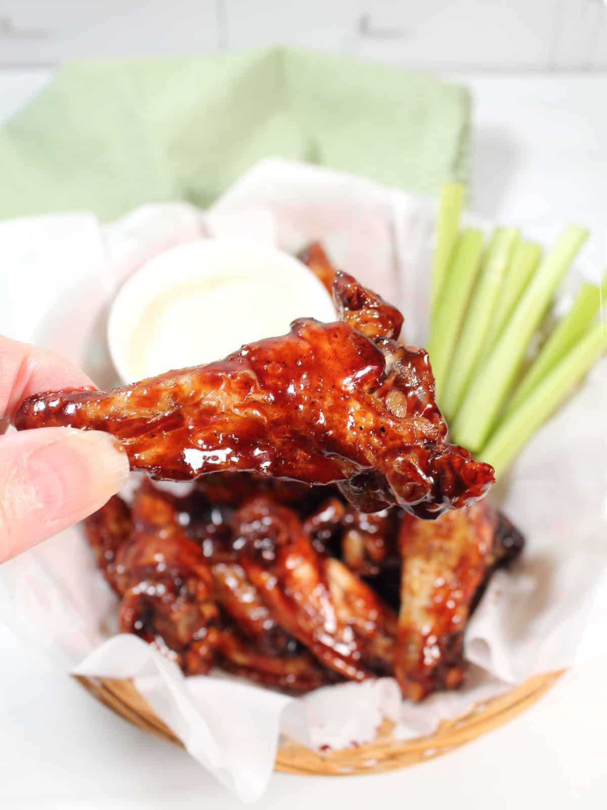 Holding sticky Asian wings above basket.