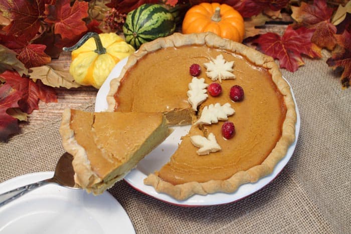 Cutting a slice of pie on pie server with gourds in backgroundamas