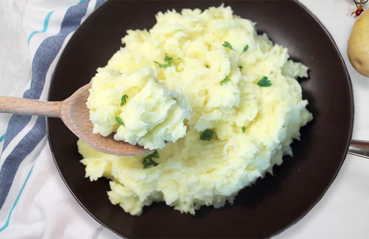 Spoonful of mashed potatoes over bowl.