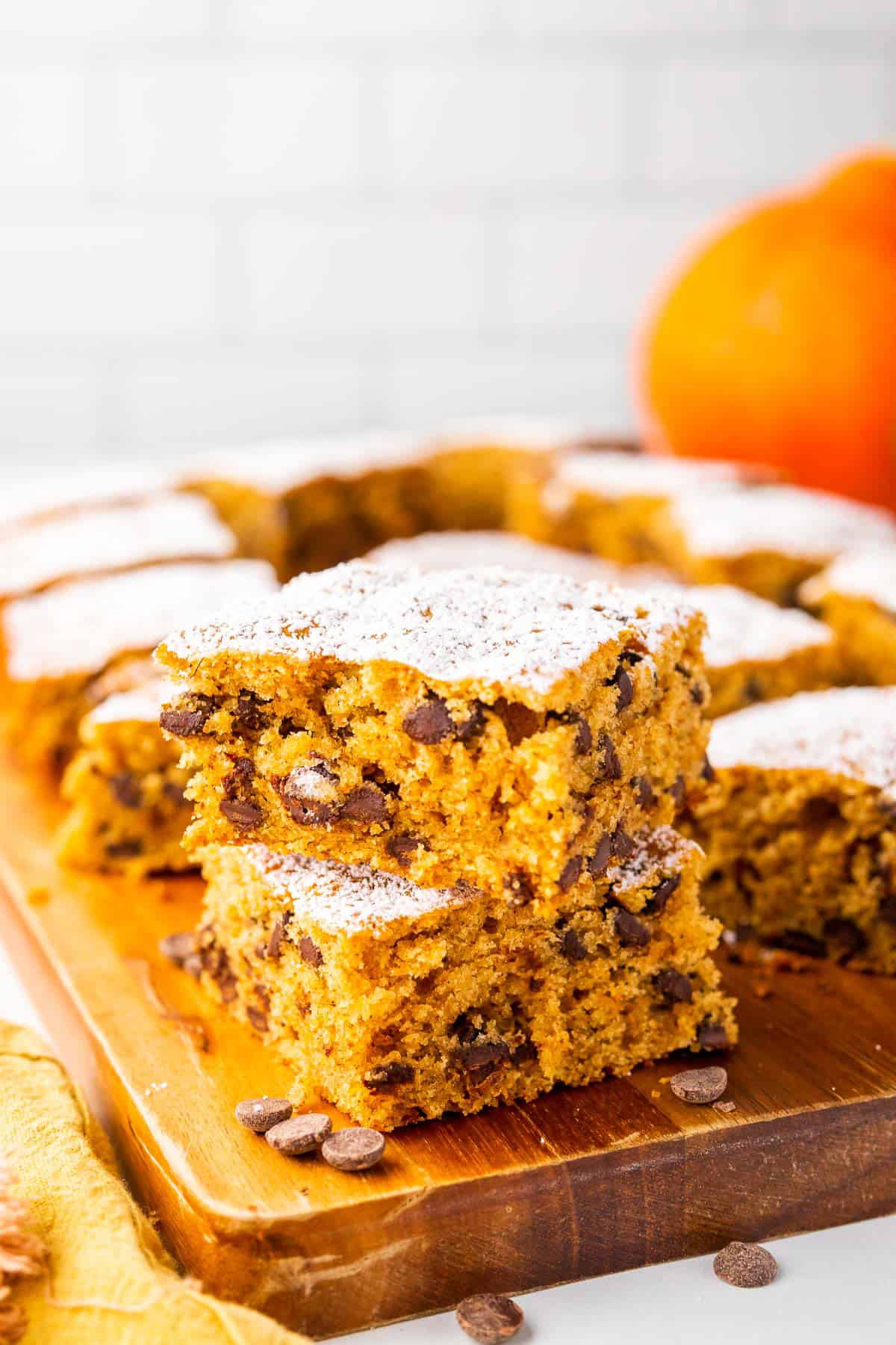 Two stacked pumpkin bars with chocolate chips on wooden board.
