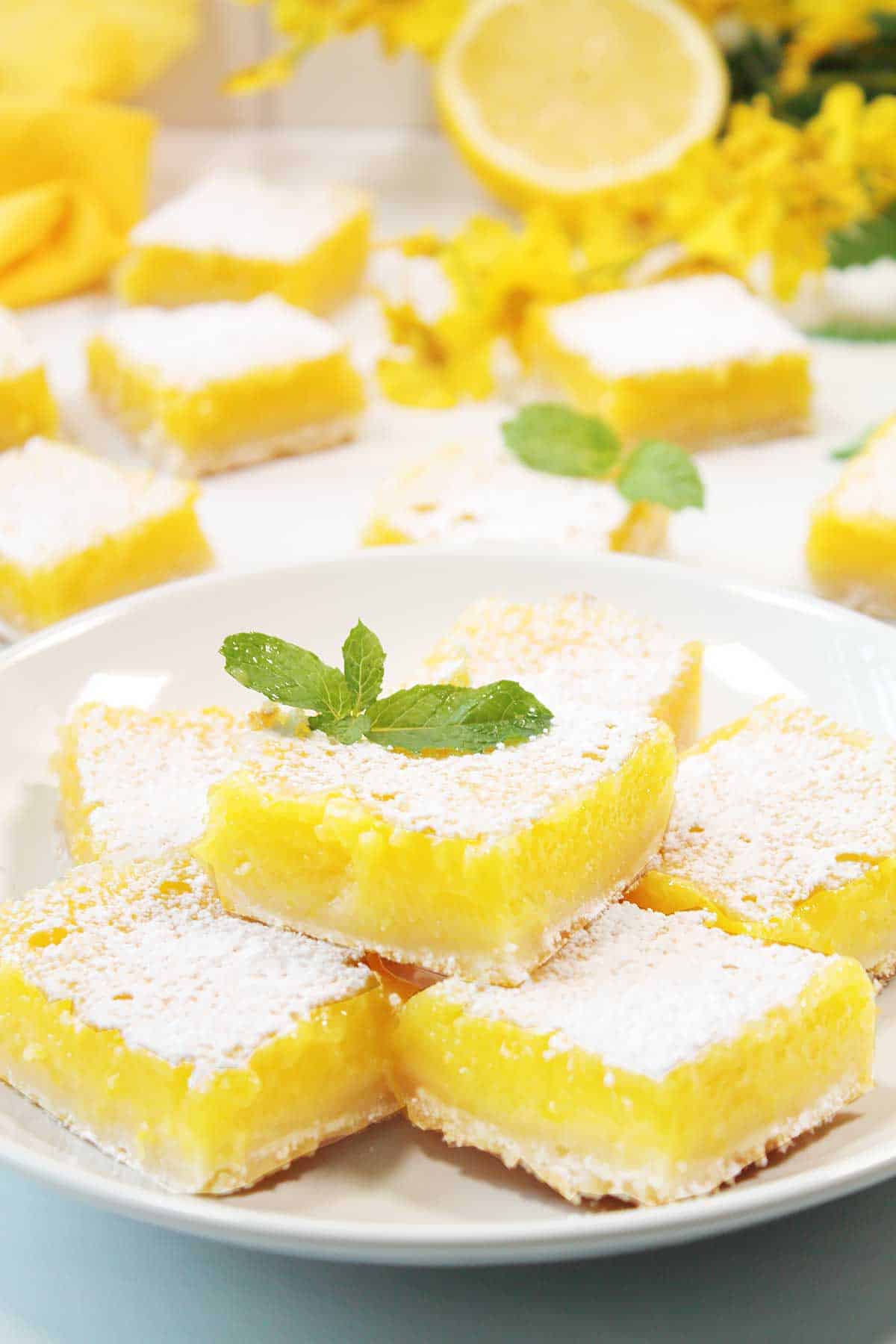 Lemon bars stacked on white plate with mint garnish.