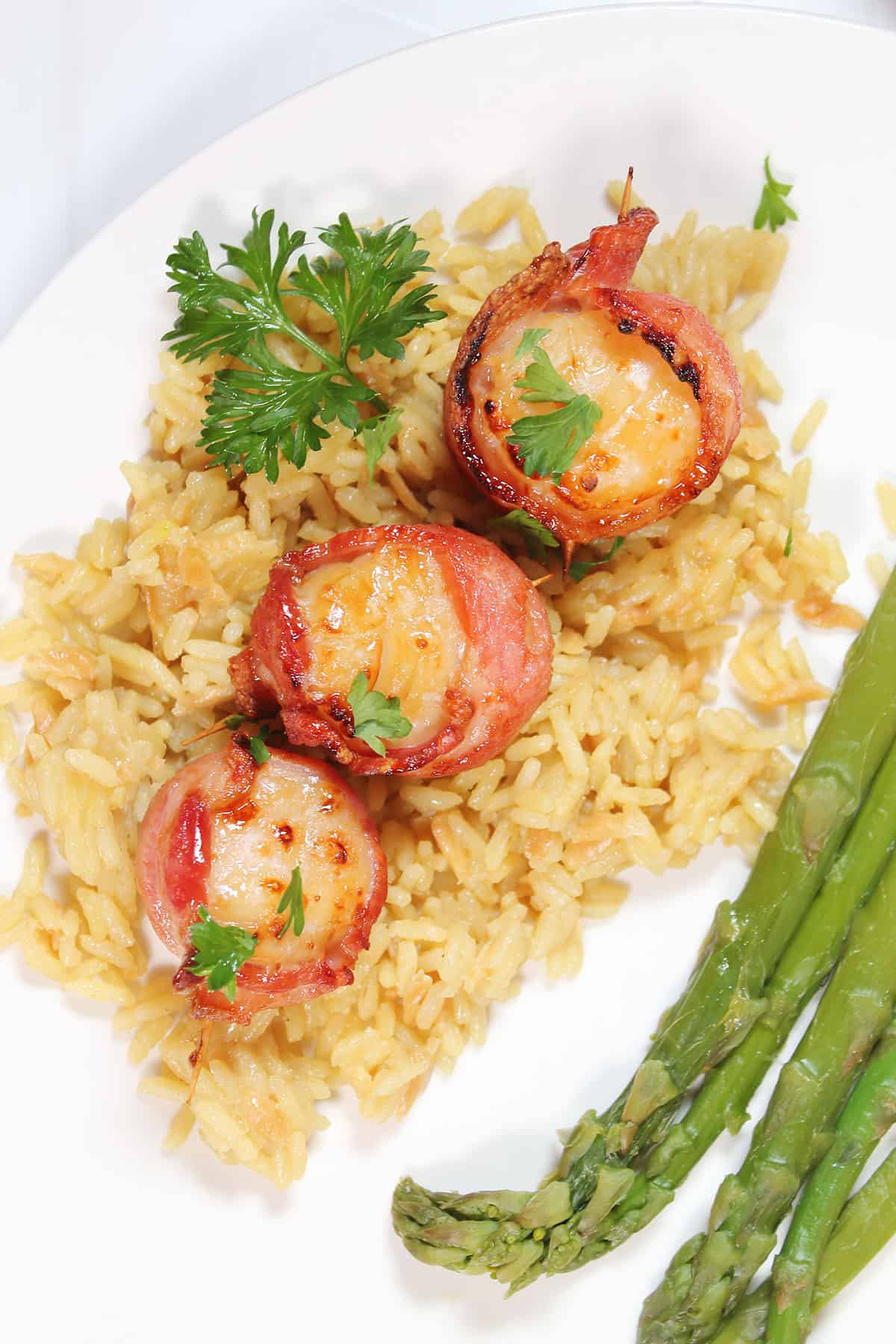 Plated bacon wrapped scallops on a bed of rice with asparagus.
