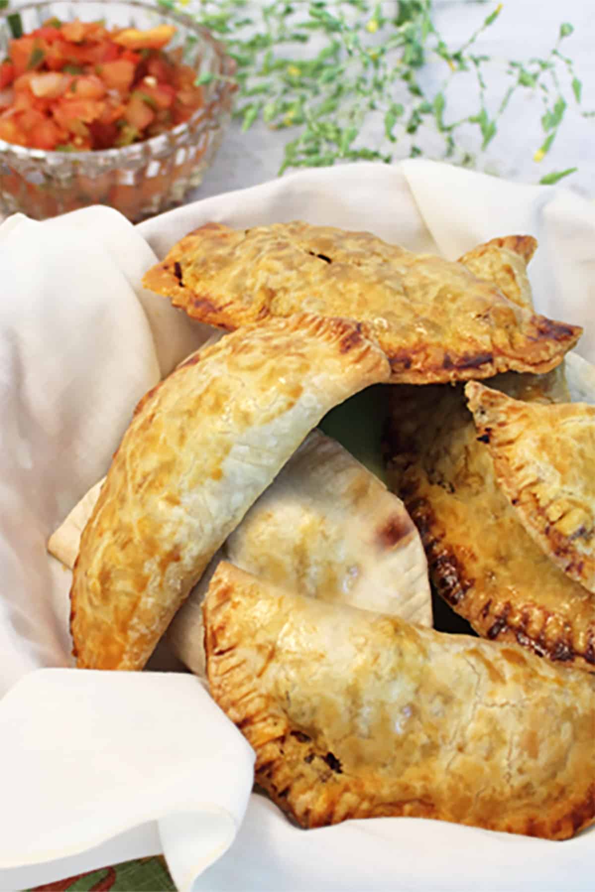 Beef empanadas in white lined basket with salsa in back.