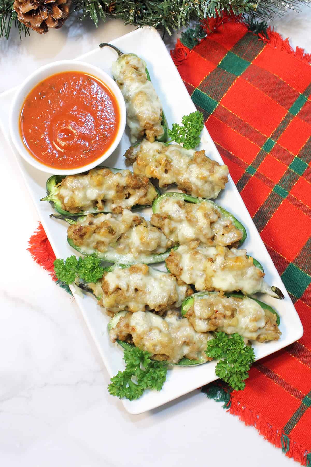 Overhead of stuffed jalapeno poppers with sausage on white serving plate with red plaid placemat.