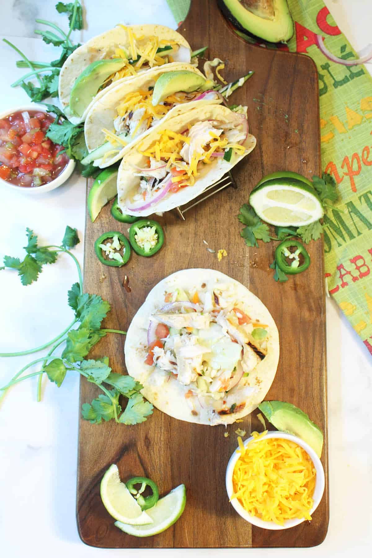 3 fish tacos in tortillas on wooden board with one open one in front.