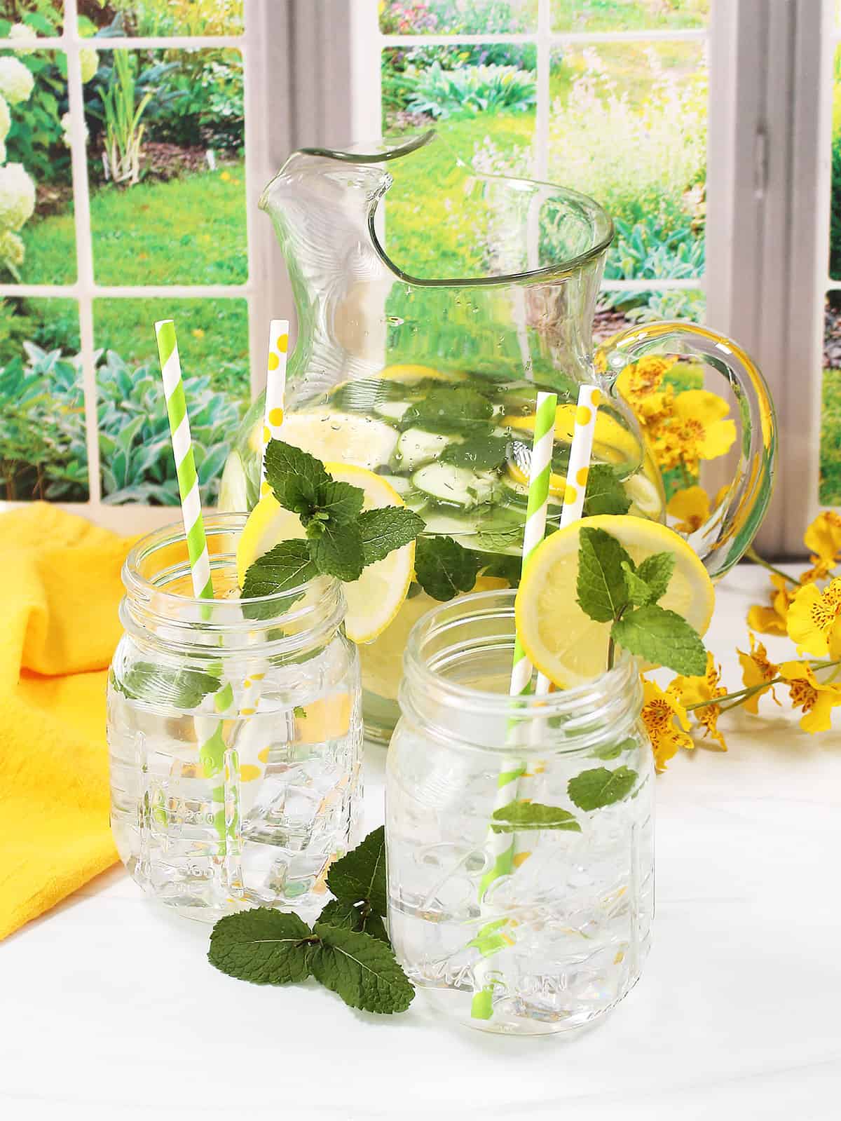 Pitcher of lemon water with cucumber in pitcher and two mason jars.
