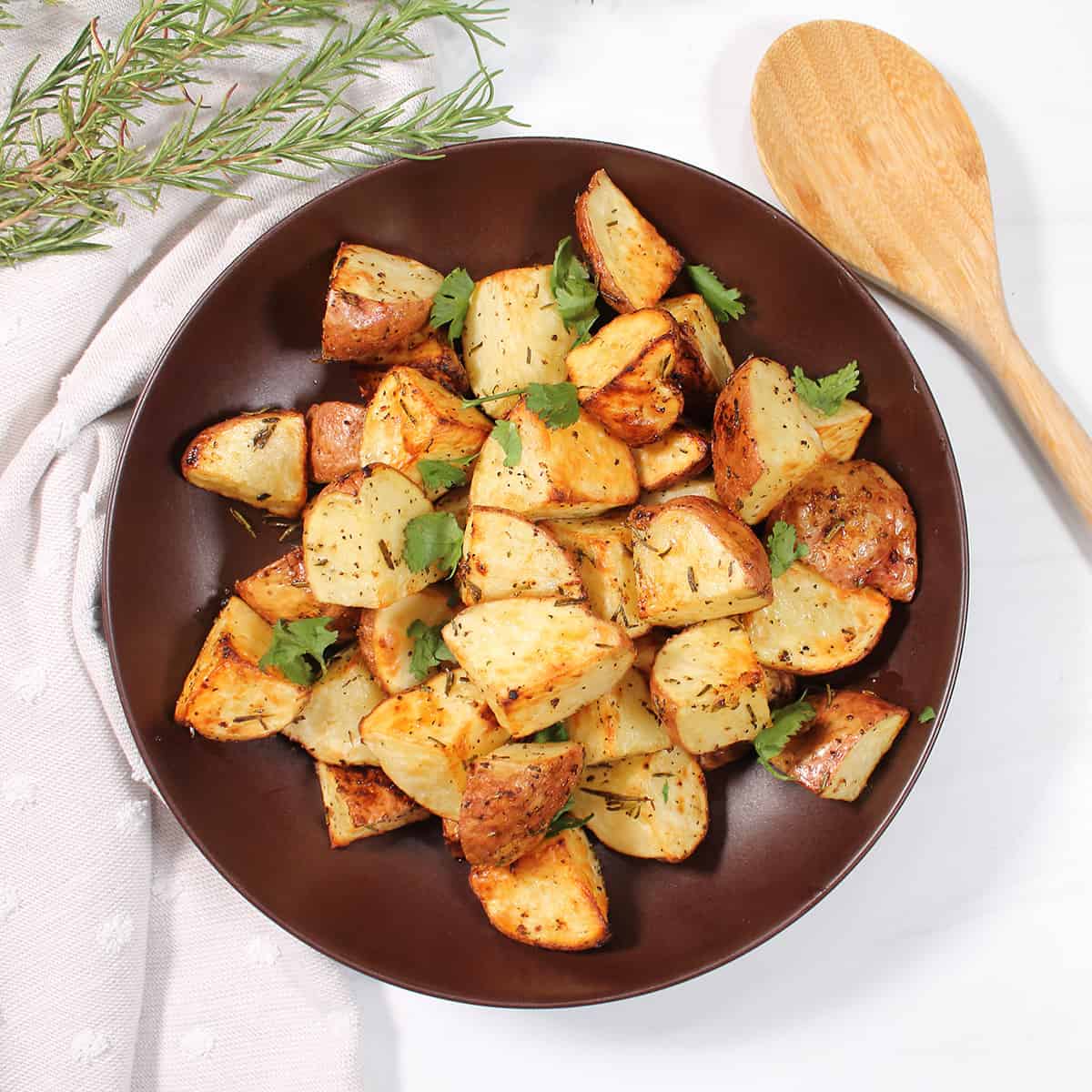 Garnished rosemary potatoes in brown bowl.