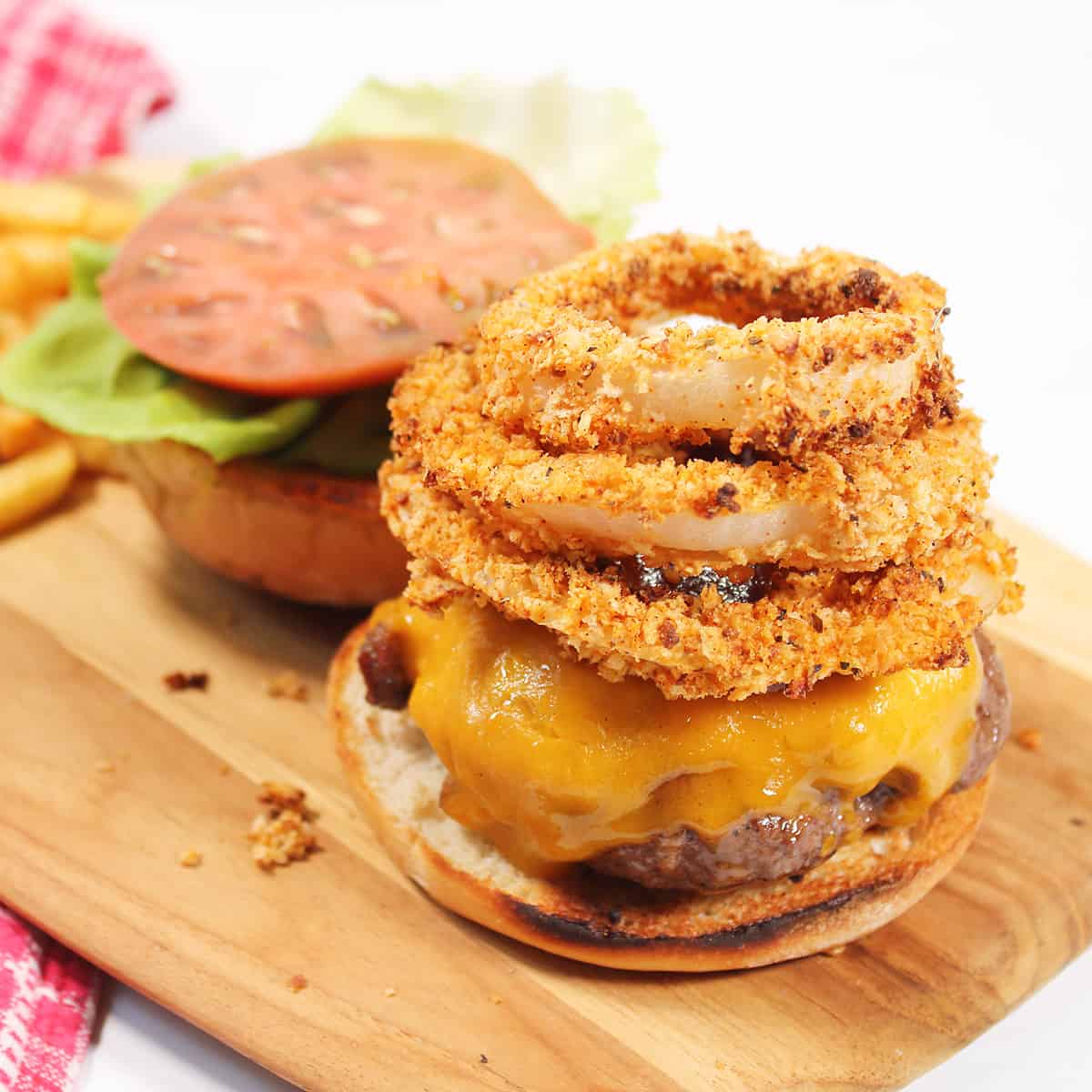 Rodeo Burger topped with onion rings on wooden board.