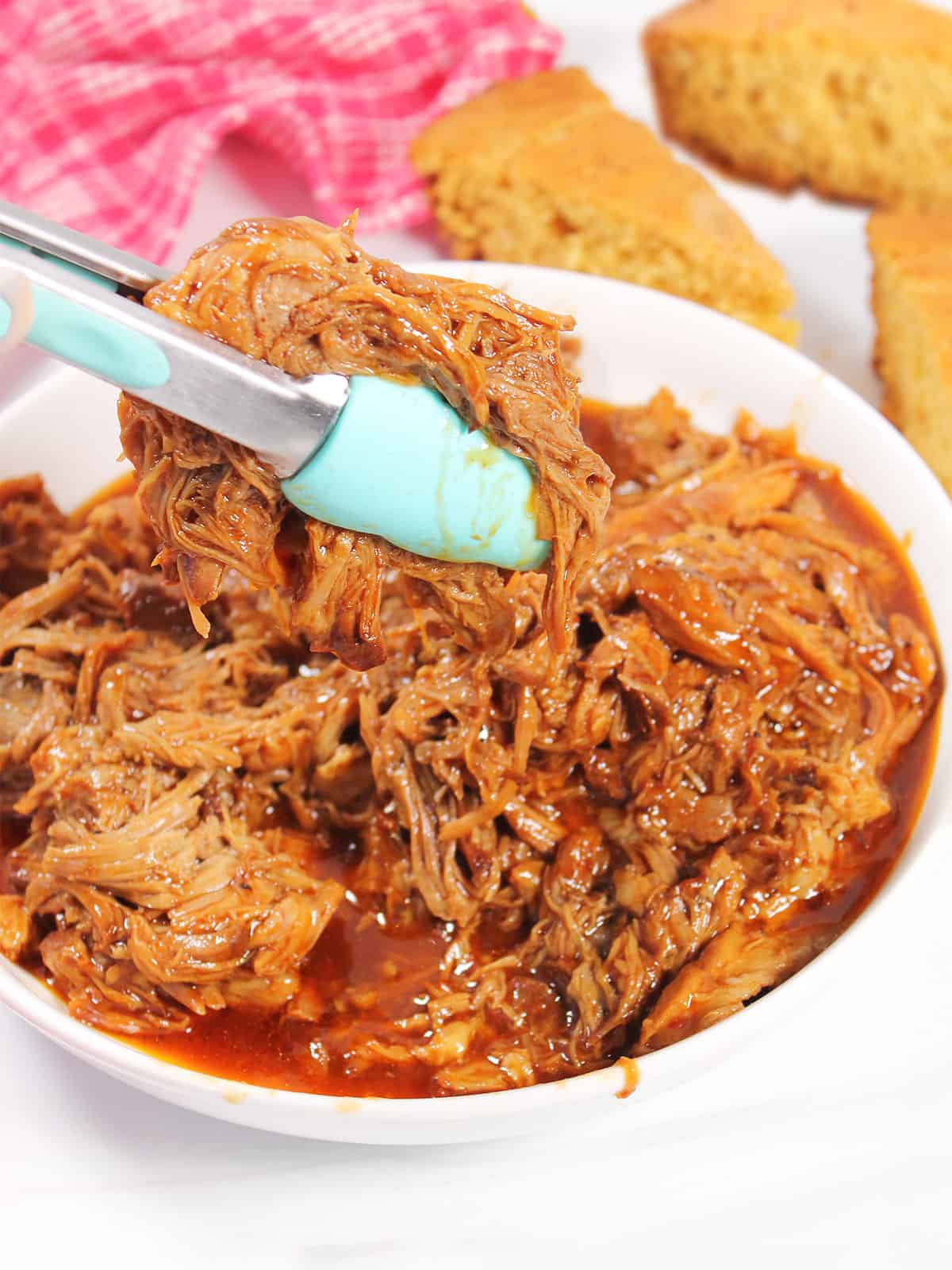 Liftin 2-ingredient slow cooker BBQ pulled pork out of bowl with tongs.