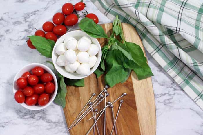 Gathered ingredients for making appetizer. Mozzarella balls, cherry tomatoes and fresh basil on wooden board.