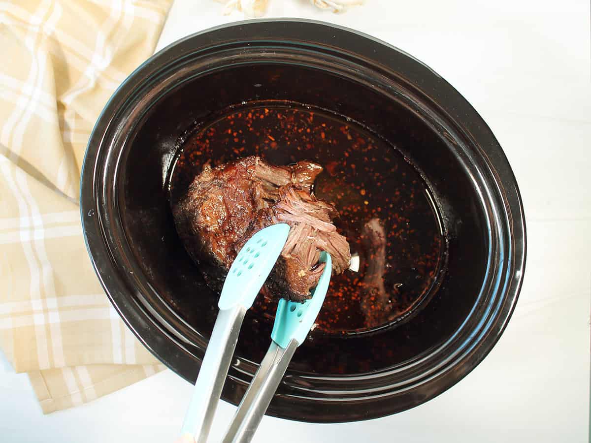 Pulling apart short ribs with tongs to show tendersness.