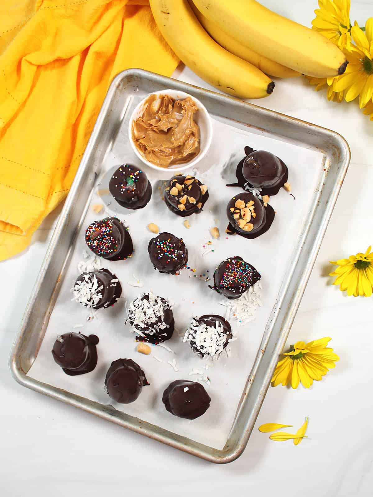 Overhead of chocolate covered frozen bananas with bowl of peanut butter.