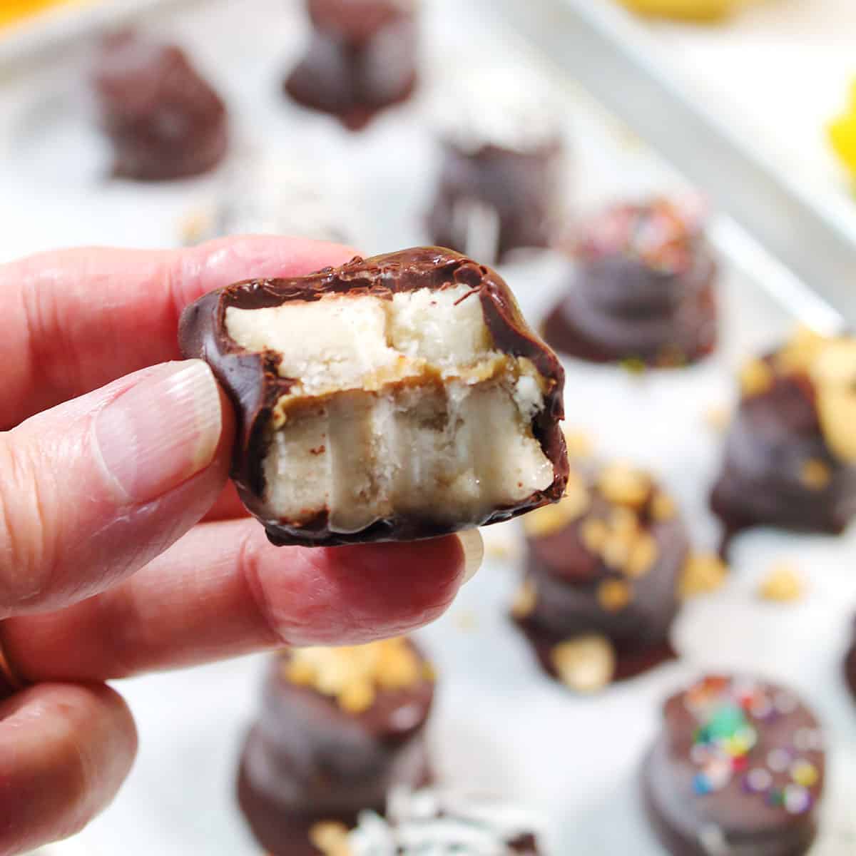 Holding frozen chocolate covered banana with bite out.