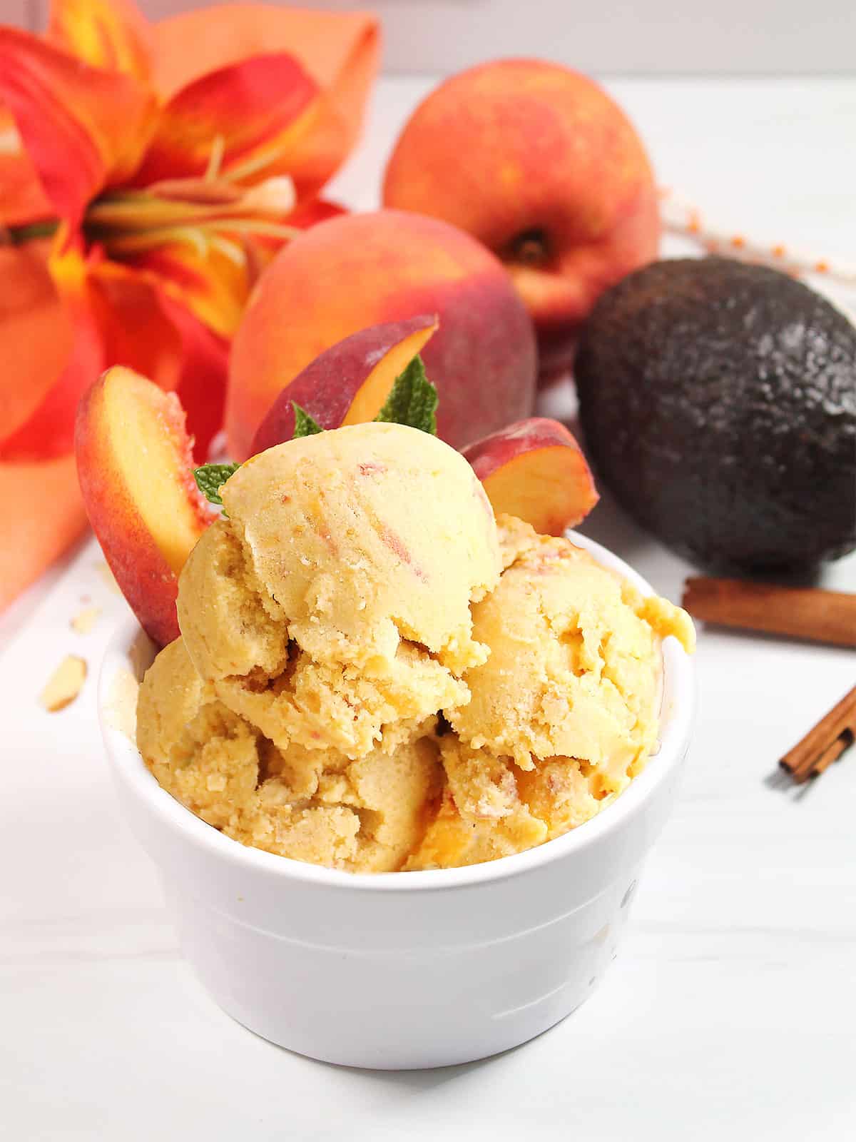 Peach ice cream in bowl with fresh peaches.