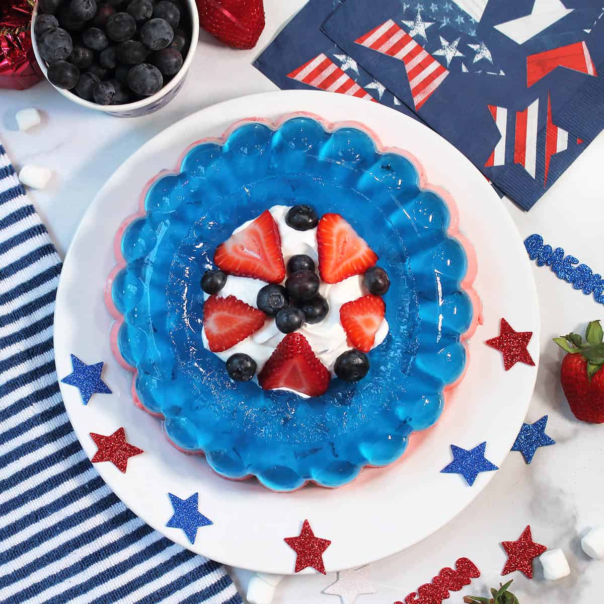 Overhead of red white and blue jello salad with patriotic napkins and blueberries.