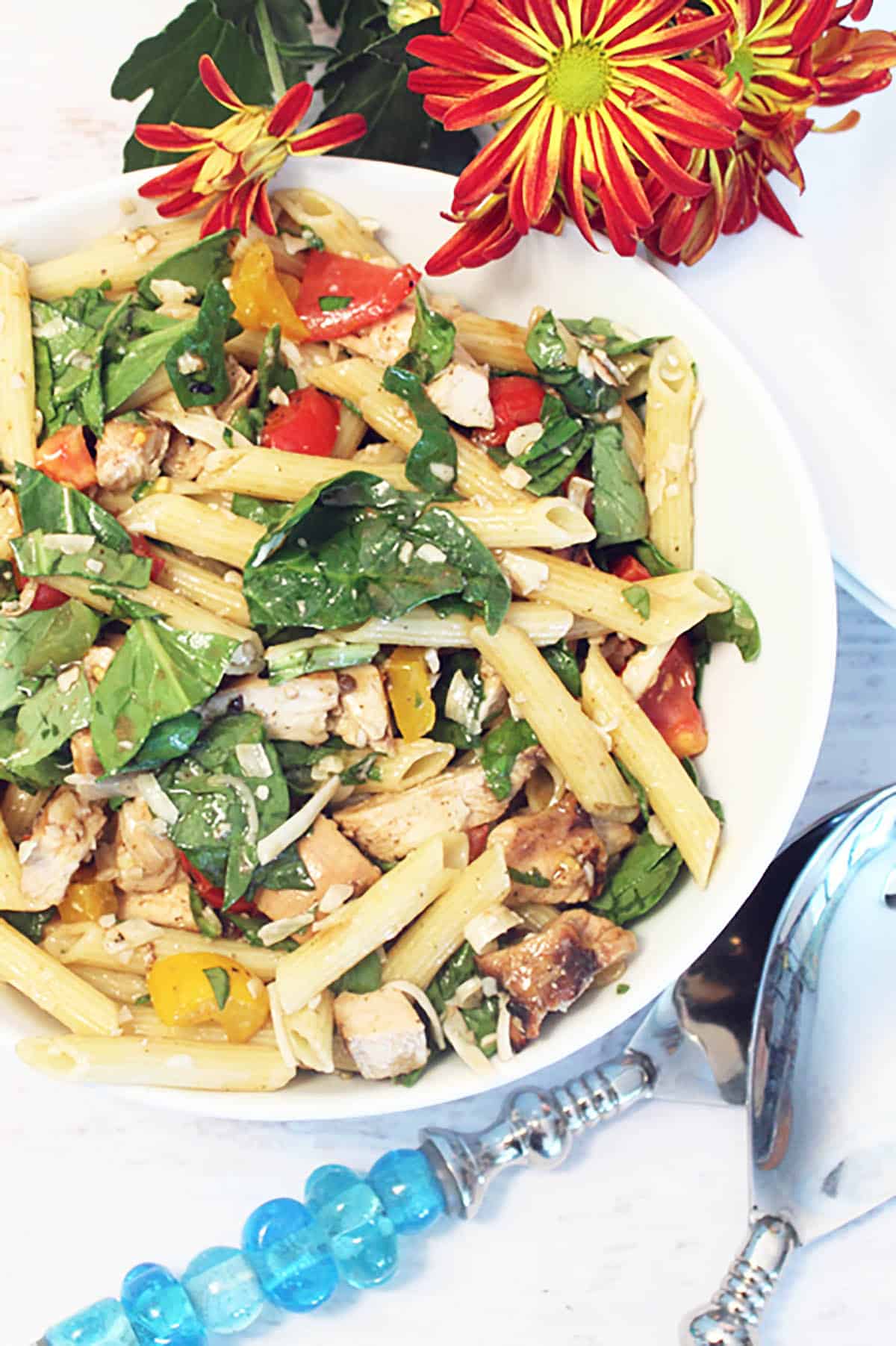 Chicken Pasta Salad in bowl with red flowers and blue handled servers.