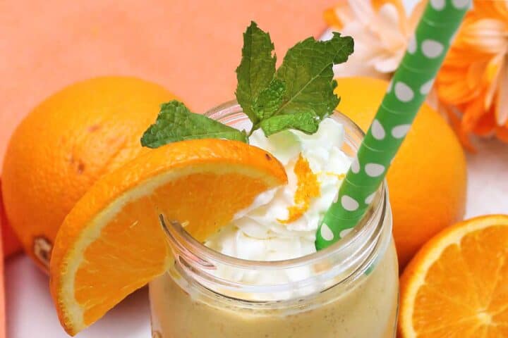 Closeup of top of smoothie with whipped cream, mint leaf and slice of orange.