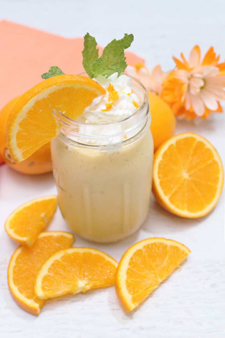 Orange Creamsicle Smoothie on white table with orange slices around it.