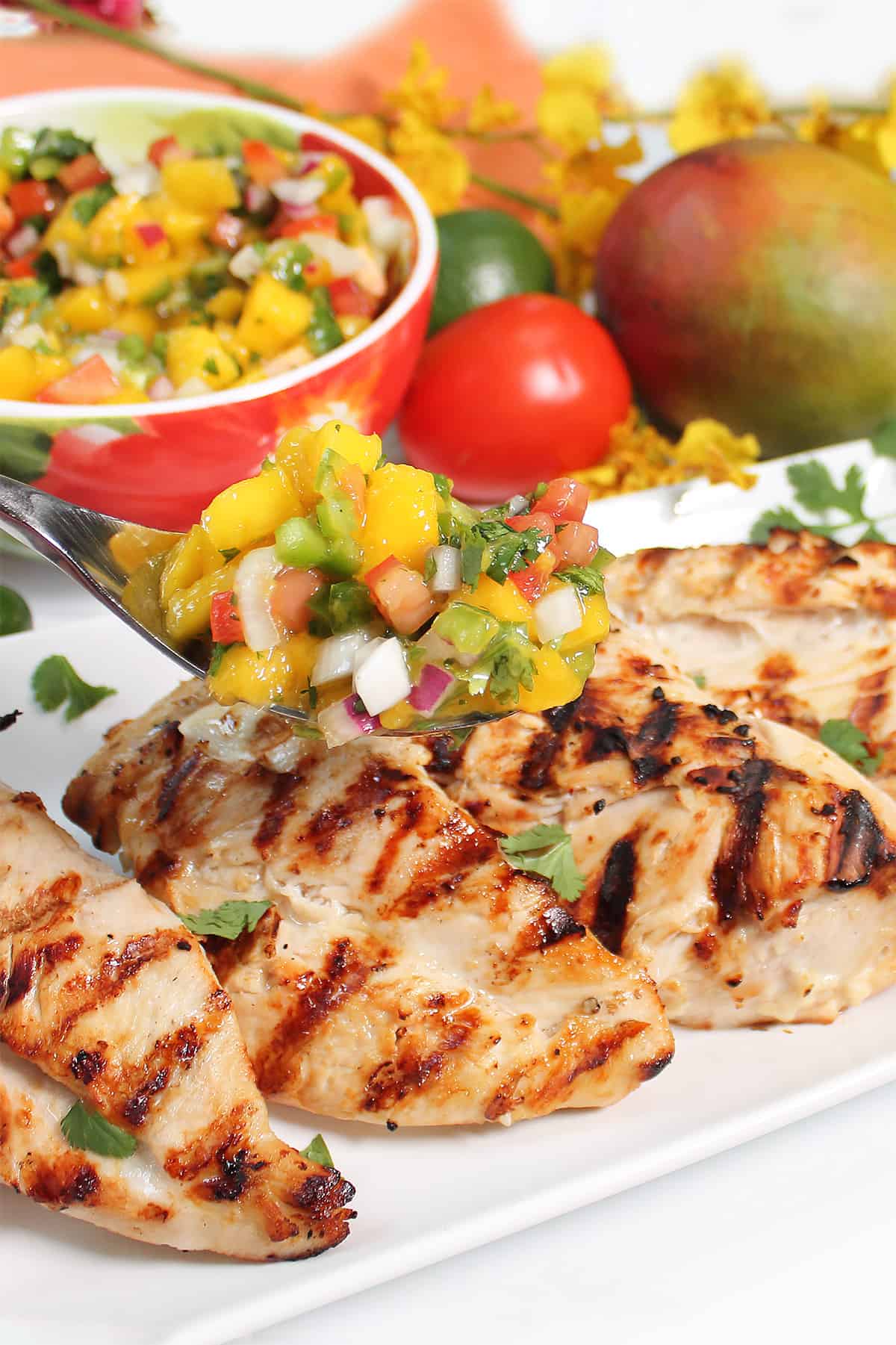 Topping lime chicken with spoonful of mango salsa.