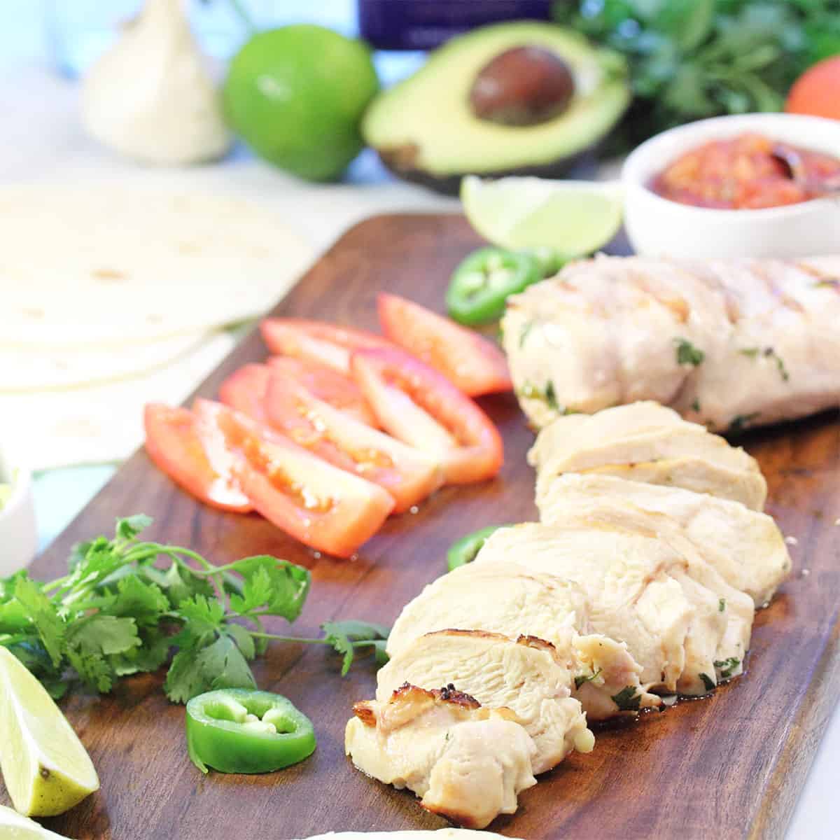 Chicken dinner on wooden board with avocado lime and tequila behind it.