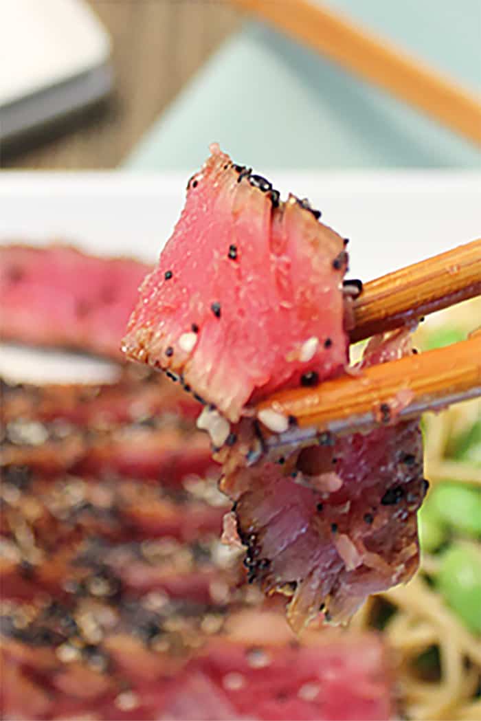 Bite of seared tuna on chopsticks.