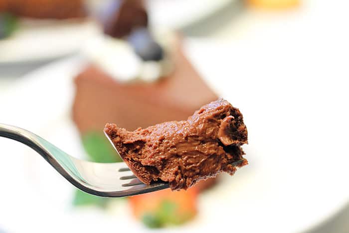 Bite of truffle cheesecake on fork with slice in background.