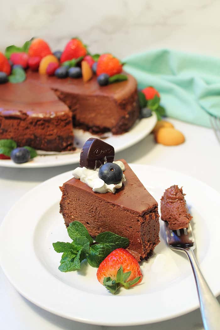 Cheesecake slice on white plate with cut cheesecake in background.
