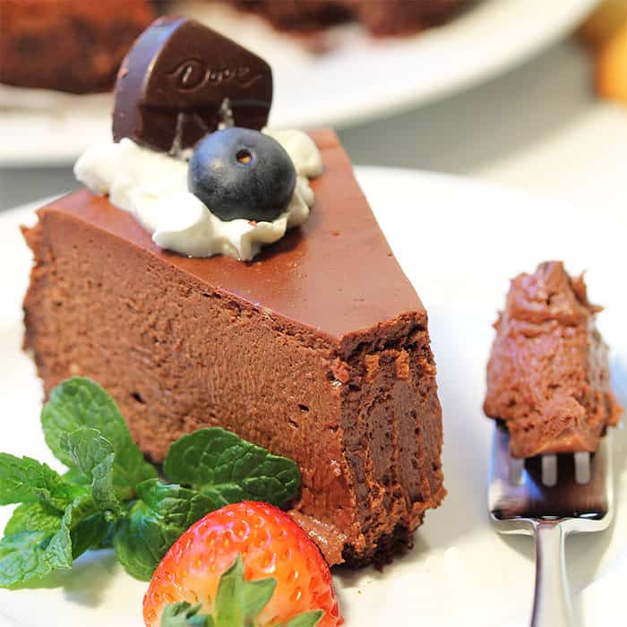 Closeup of slice on white plate with forkful decorated with whipped cream and a chocolate