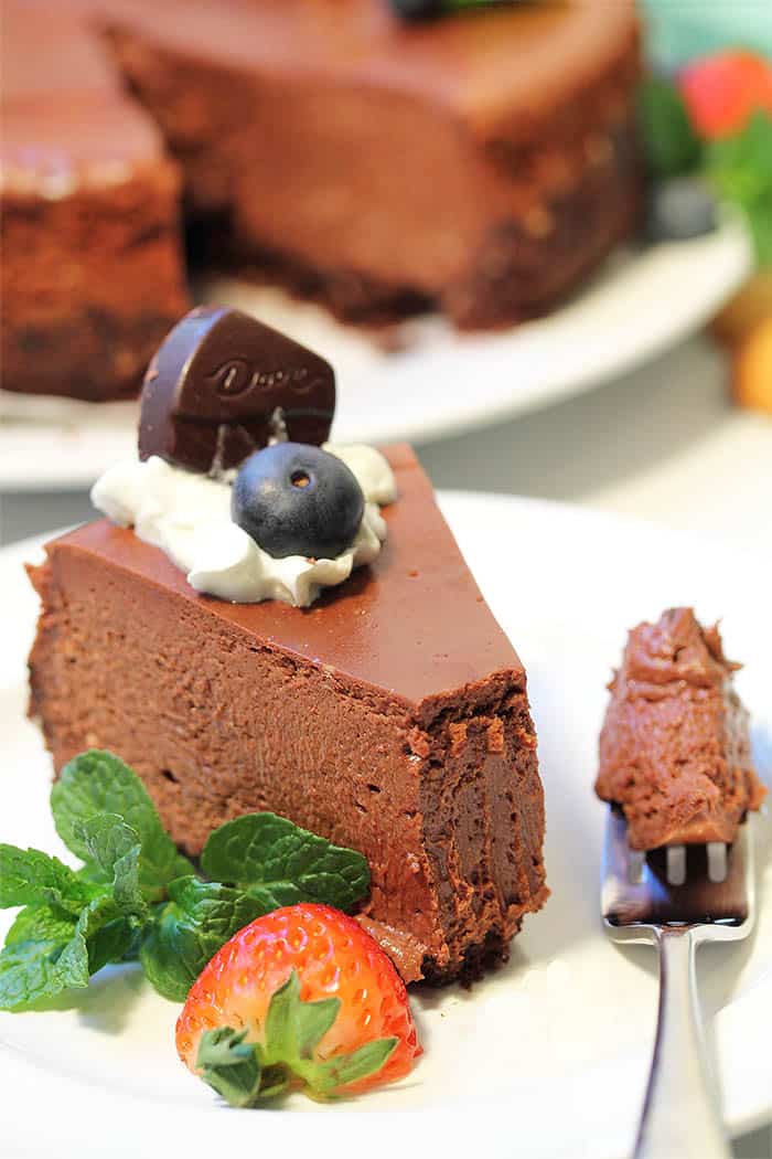 Closeup of chocolate cheesecake slice on white plate with forkful on side.