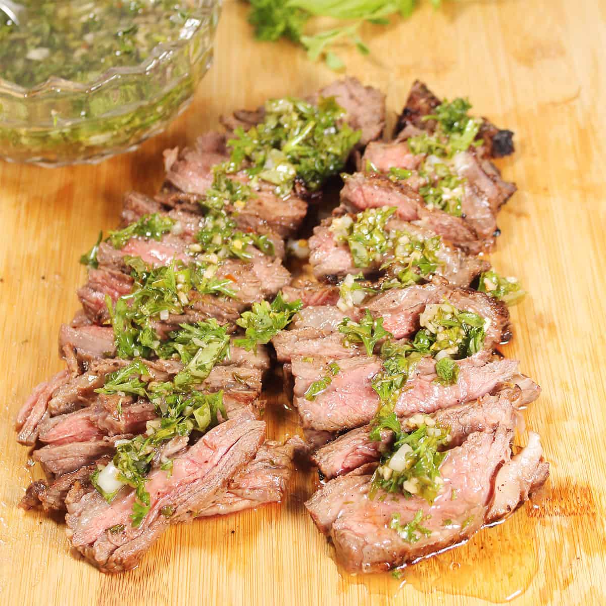 Sliced grilled steak with chimichurri sauce on cutting board.