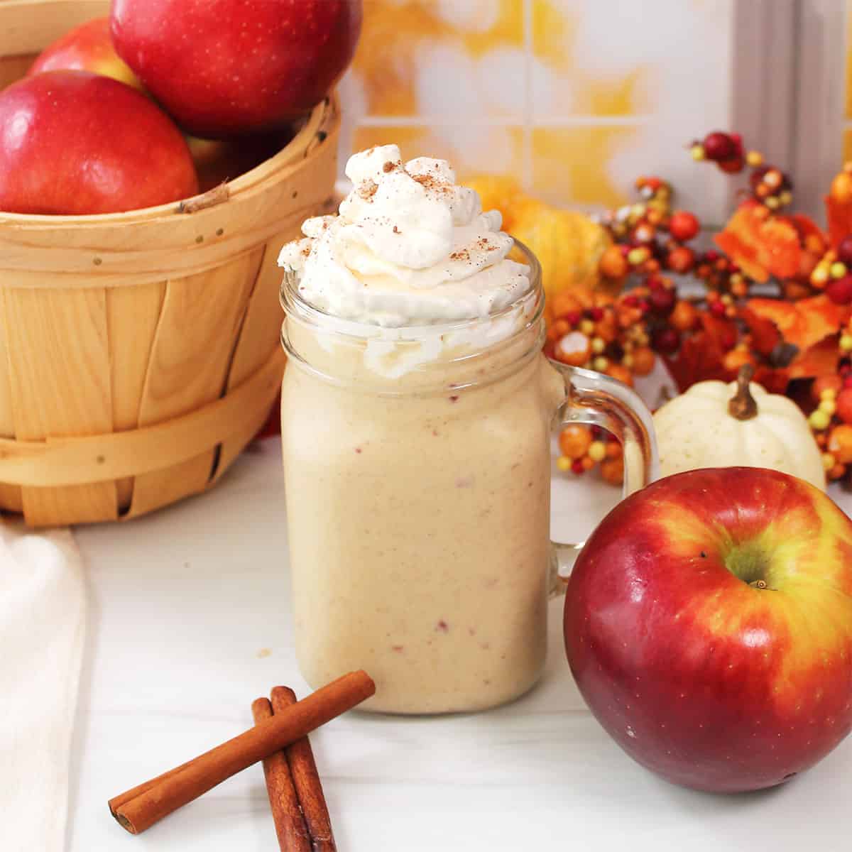 Apple Pie Smoothie with whipped cream by basket of apples.
