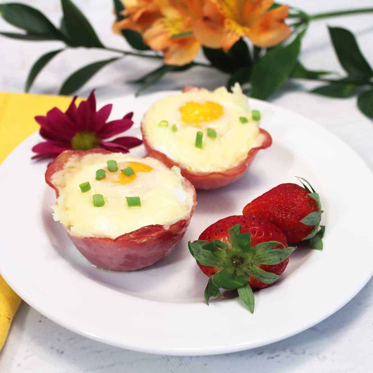 A serving of two egg cups on white plate with strawberries.